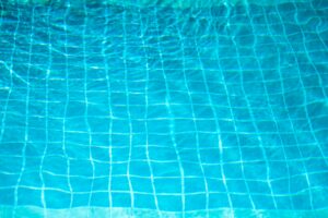 A vibrant image of blue swimming pool tiles with shimmering water reflections.