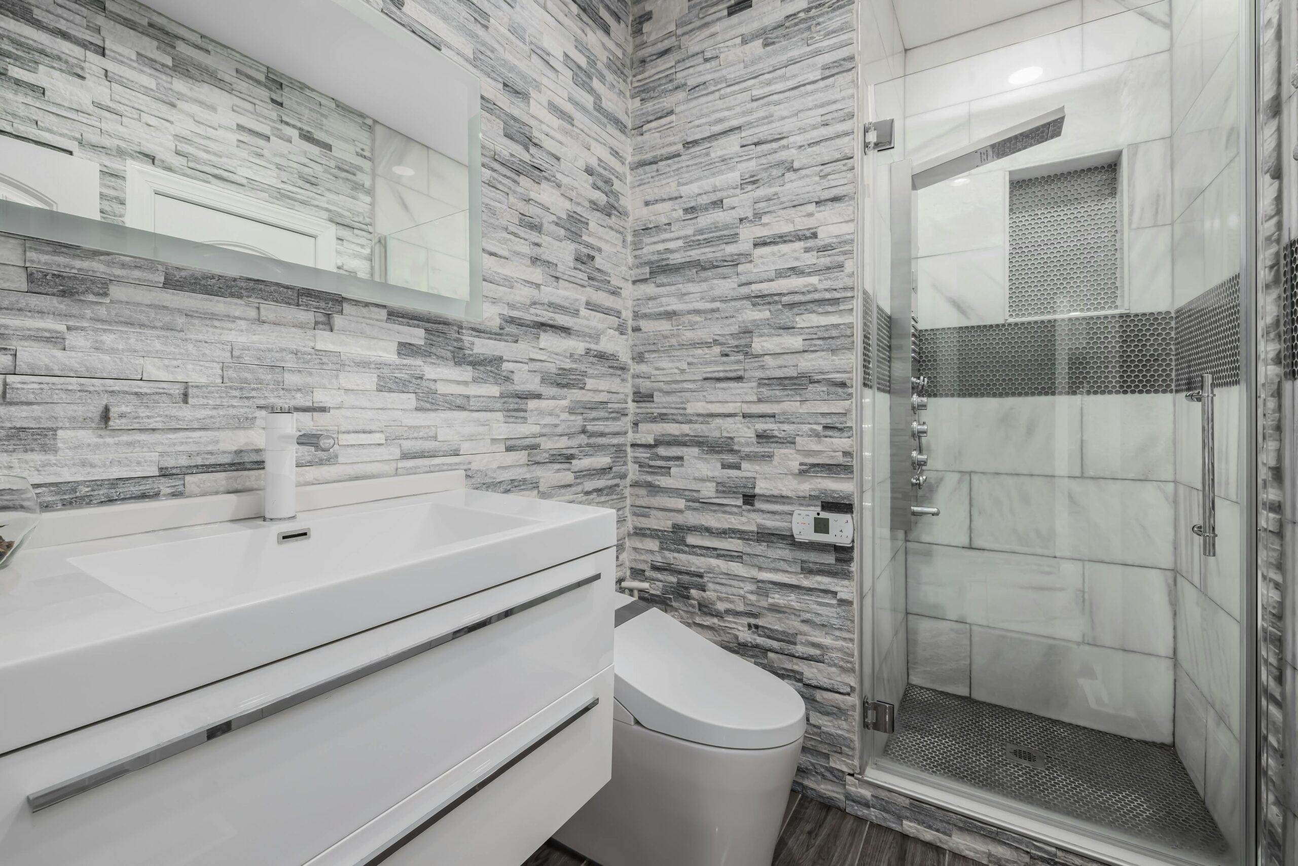 Stylish modern bathroom featuring a glass shower, stone walls, and sleek white vanity.