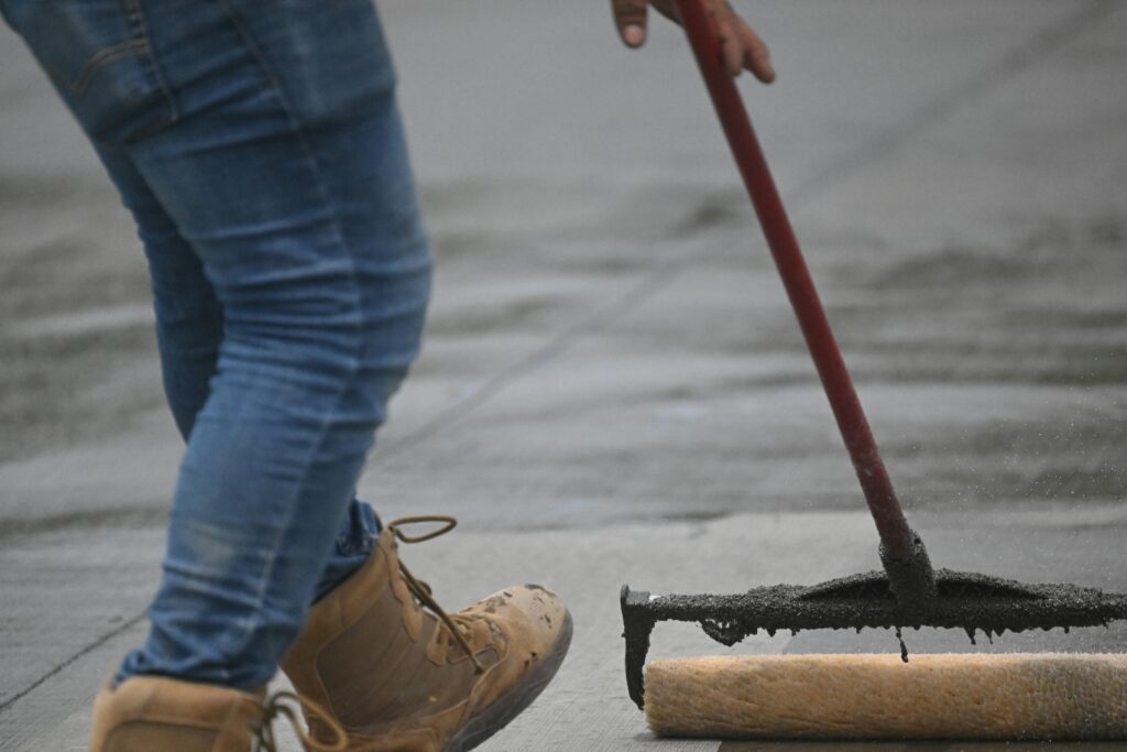 Detailed image of concrete sealing with a roller on pavement, showing boots and jeans in action.