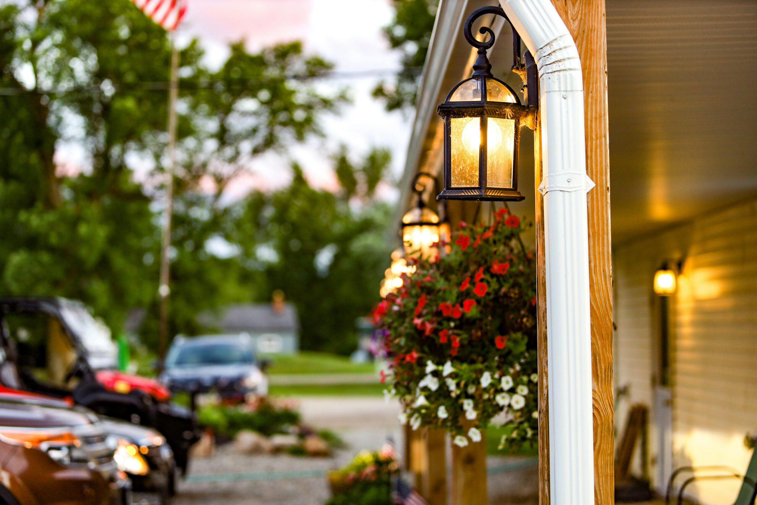 Charming illuminated porch with hanging flower baskets at dusk, creating a warm and inviting atmosphere.