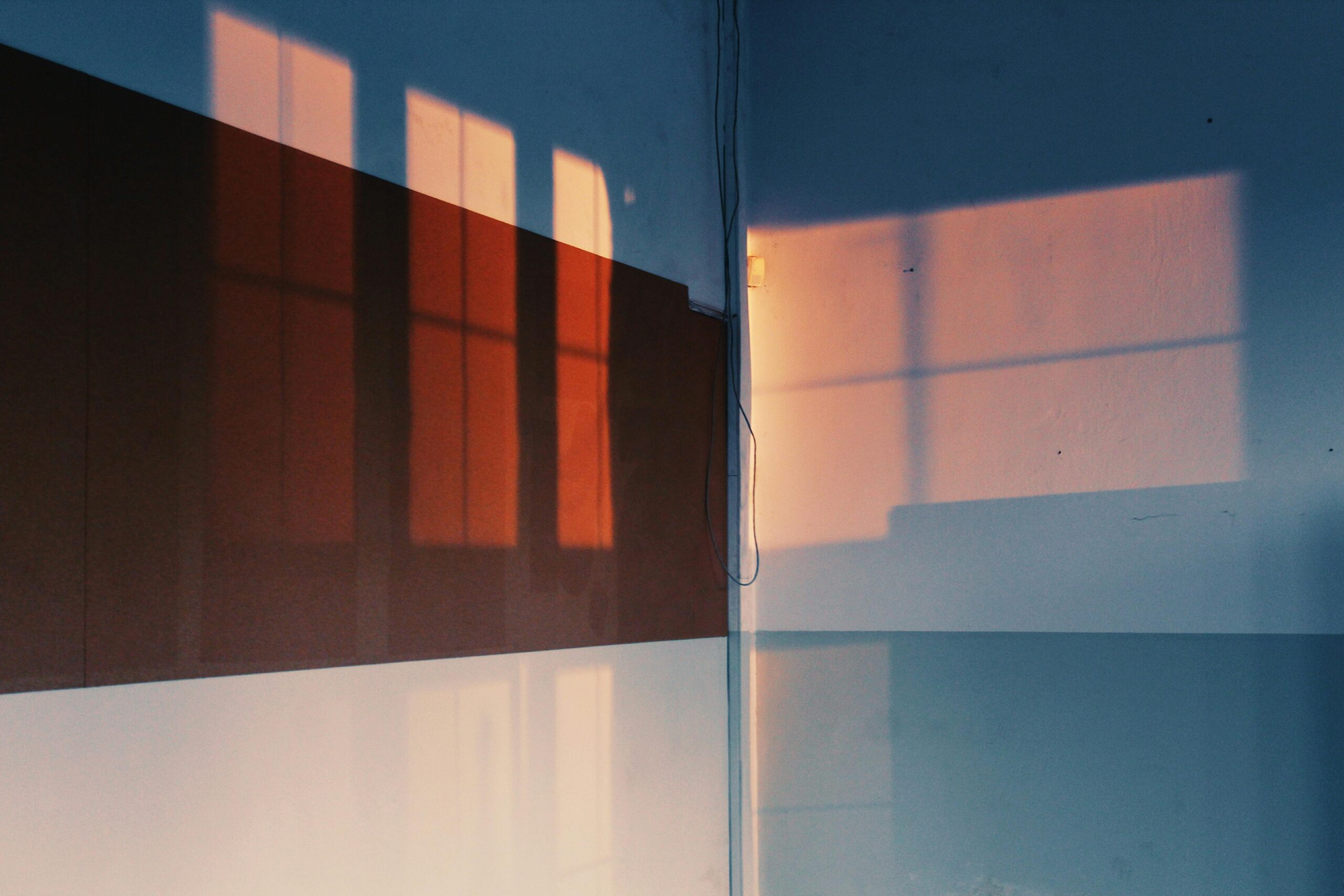 Artistic shadows of windows cast on a wall, creating a warm, intriguing pattern indoors.