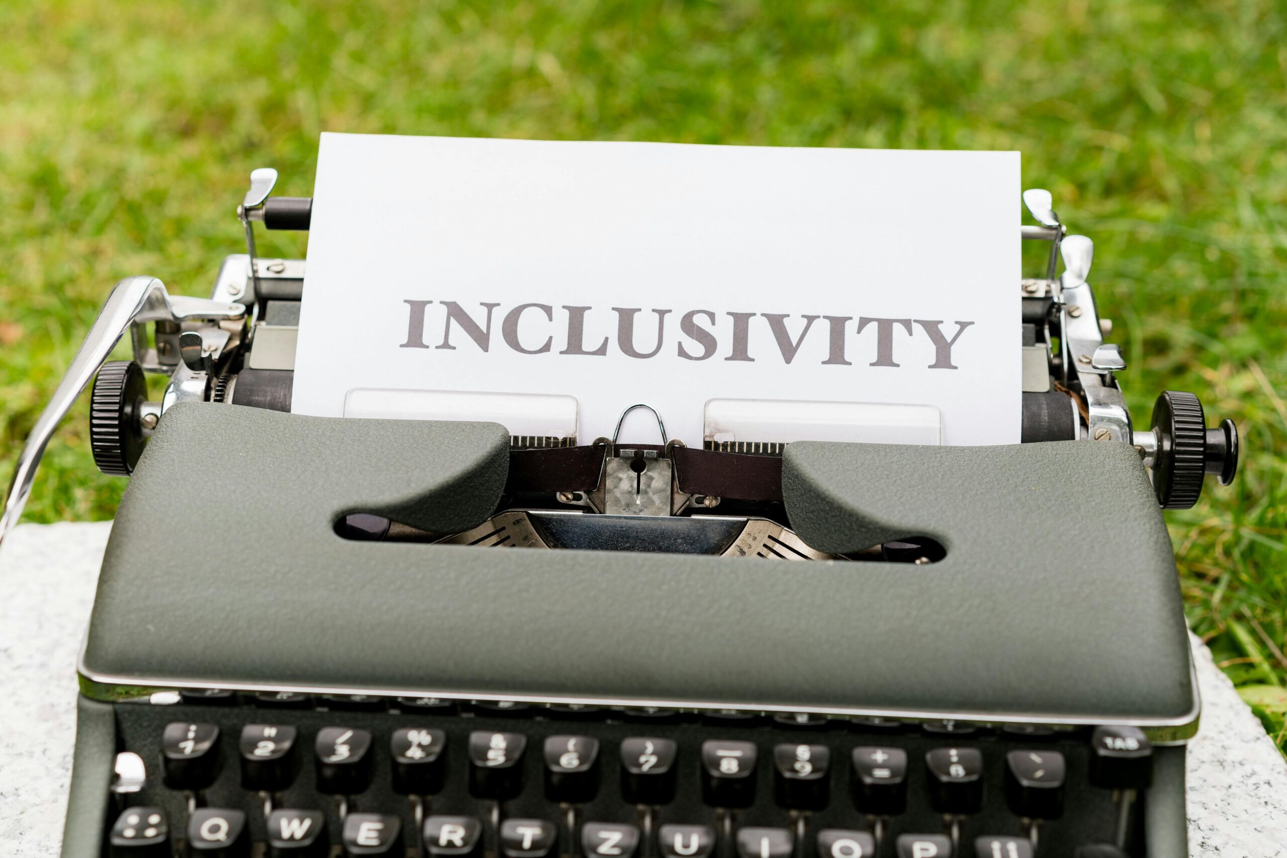 A vintage typewriter with a sheet displaying 'Inclusivity' on a lush green background.