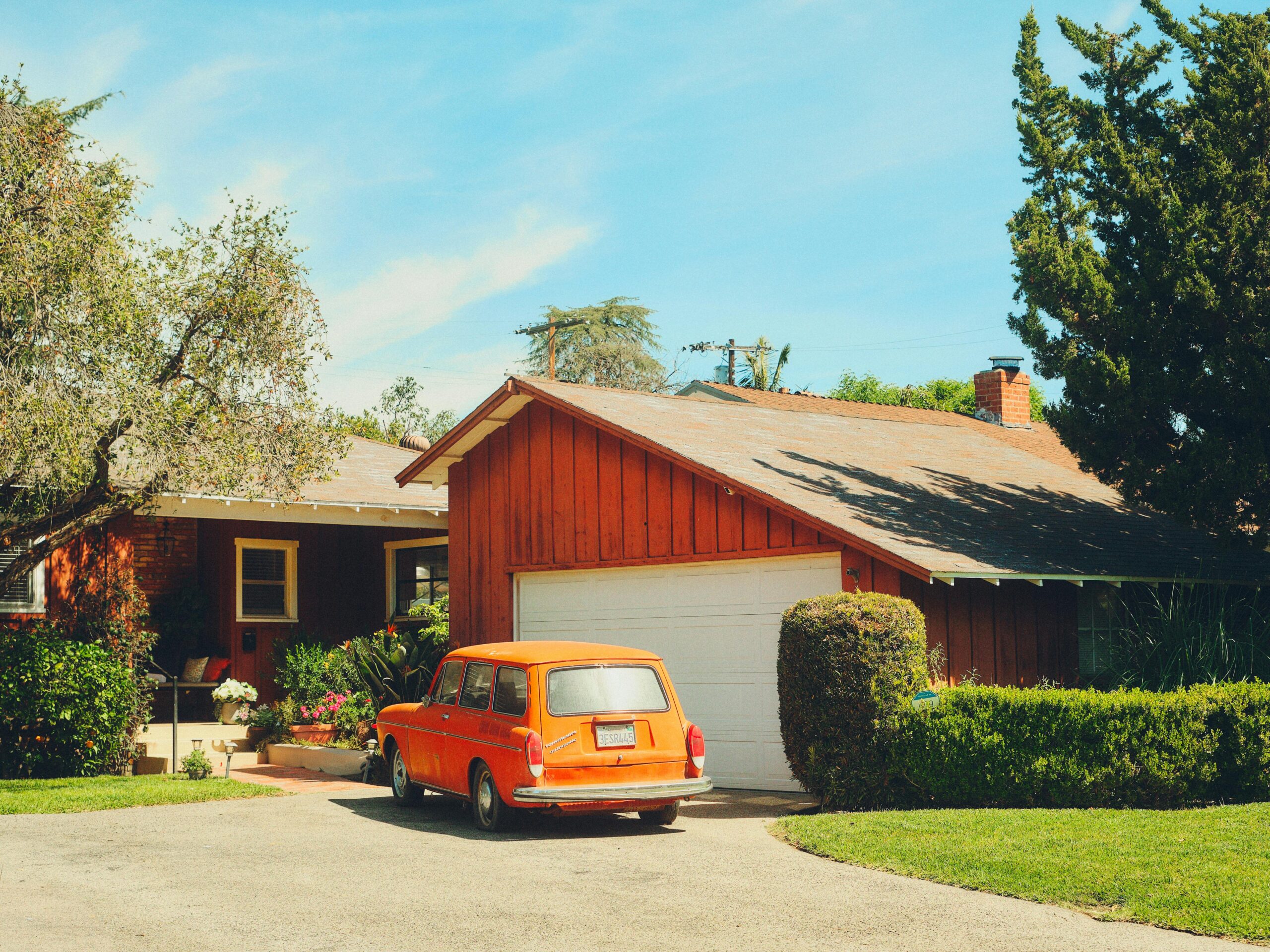 Classic orange car parked in a suburban driveway surrounded by greenery in Los Angeles.