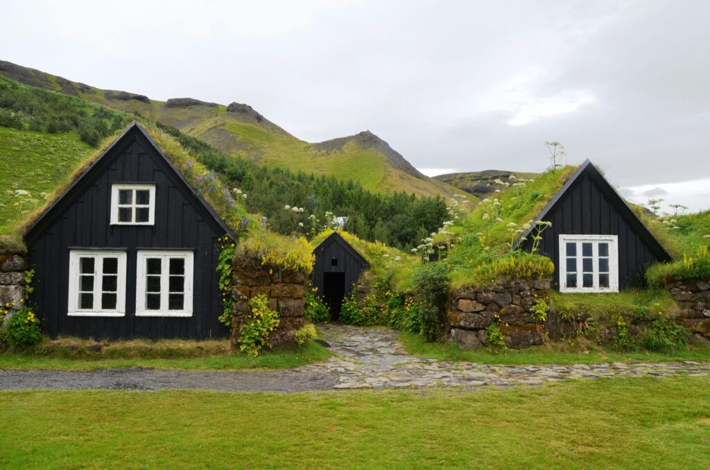 Explore the rustic charm of traditional turf roofed houses set against a lush hillside in serene countryside.