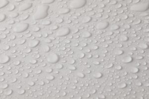 Closeup top view of plain wet abstract surface with small dripped water drops of different shapes placed on white background