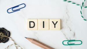 Close-up of a DIY crafting setup with paper clips, pencil, and tiles on a white surface.