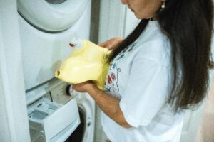 A woman pours detergent into a washing machine for a laundry cycle.