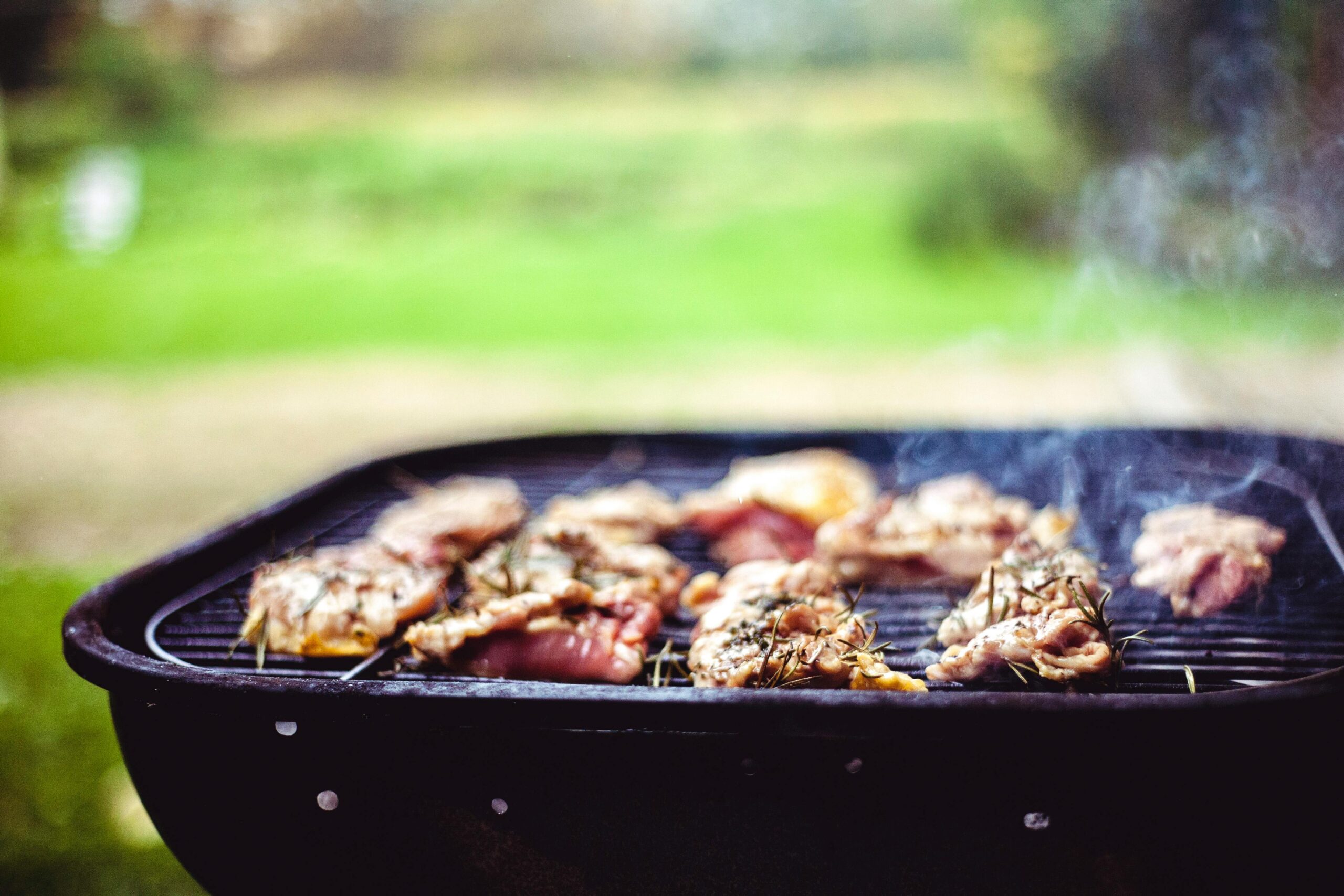 Juicy meat sizzling on a grill outdoors, seasoned with fresh rosemary for a mouthwatering meal.