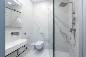 Elegant white marble bathroom featuring a sleek shower, toilet, and sink.
