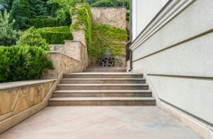 Gray concrete stairs of modern house with fresh green bushes and grass in yard
