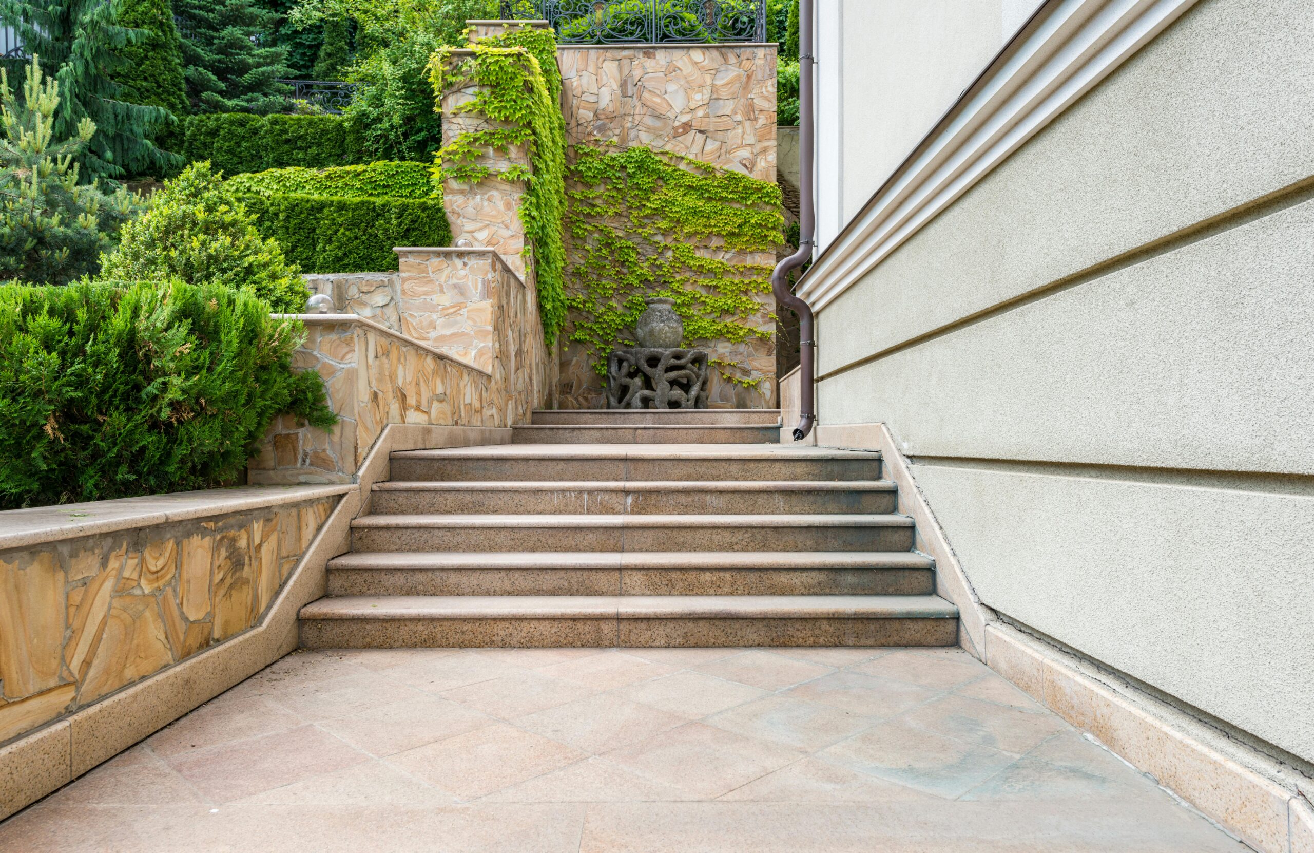 Gray concrete stairs of modern house with fresh green bushes and grass in yard