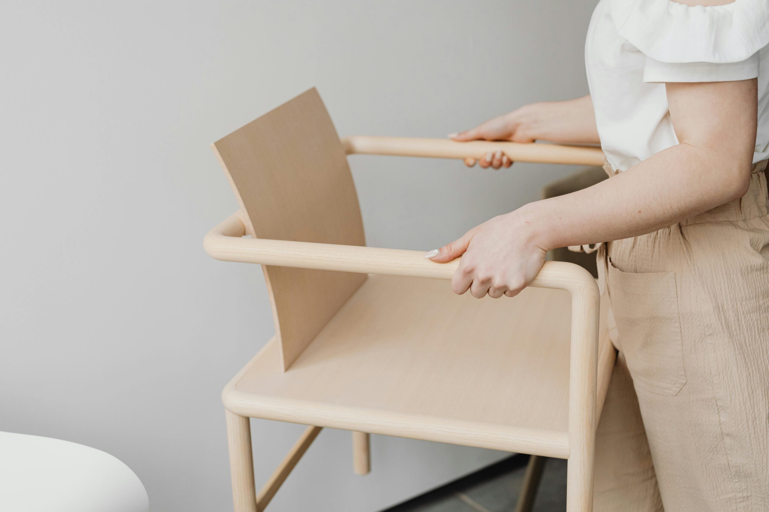 A woman holding a minimalist wooden chair, showcasing Scandinavian design