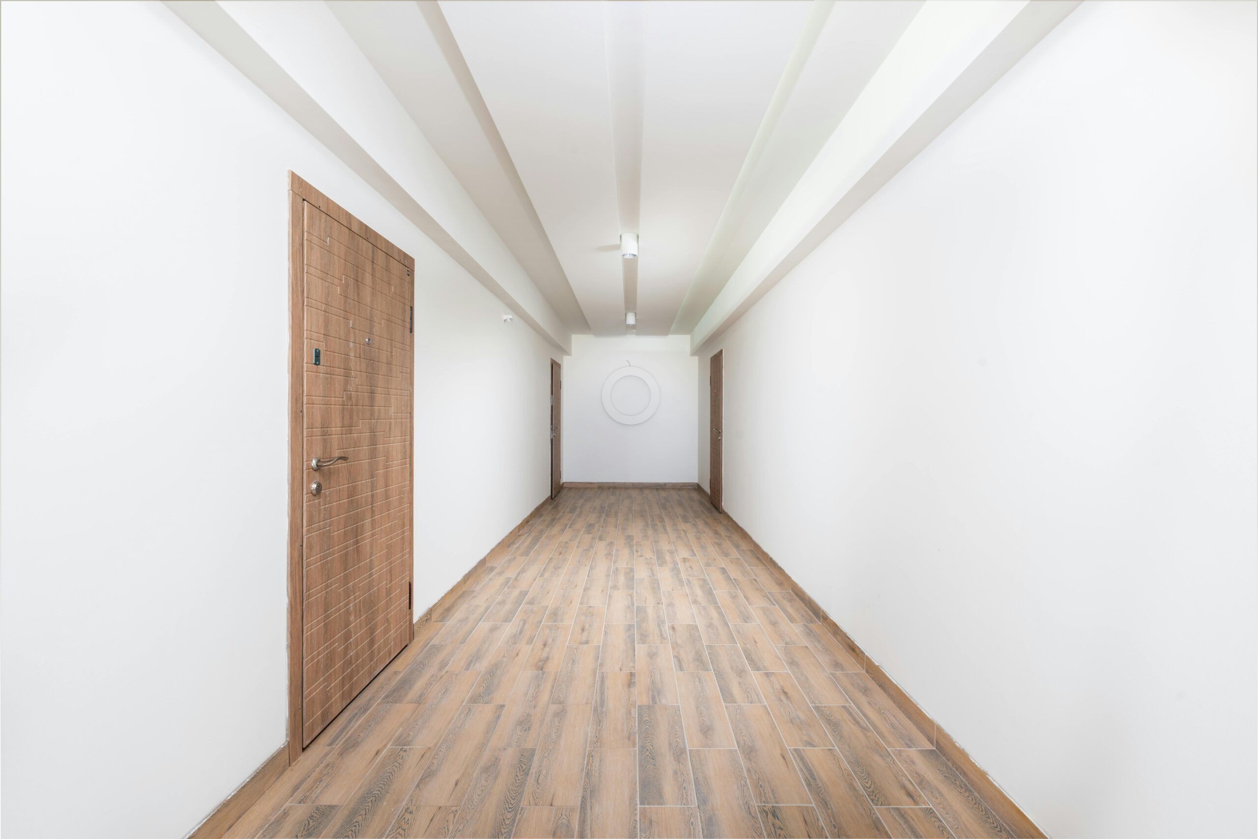 Clean white hallway with wooden flooring and contemporary doors, showcasing minimalism.