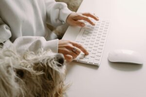 A person typing on a wireless keyboard with a fluffy dog nearby, showcasing companionship and modern technology.