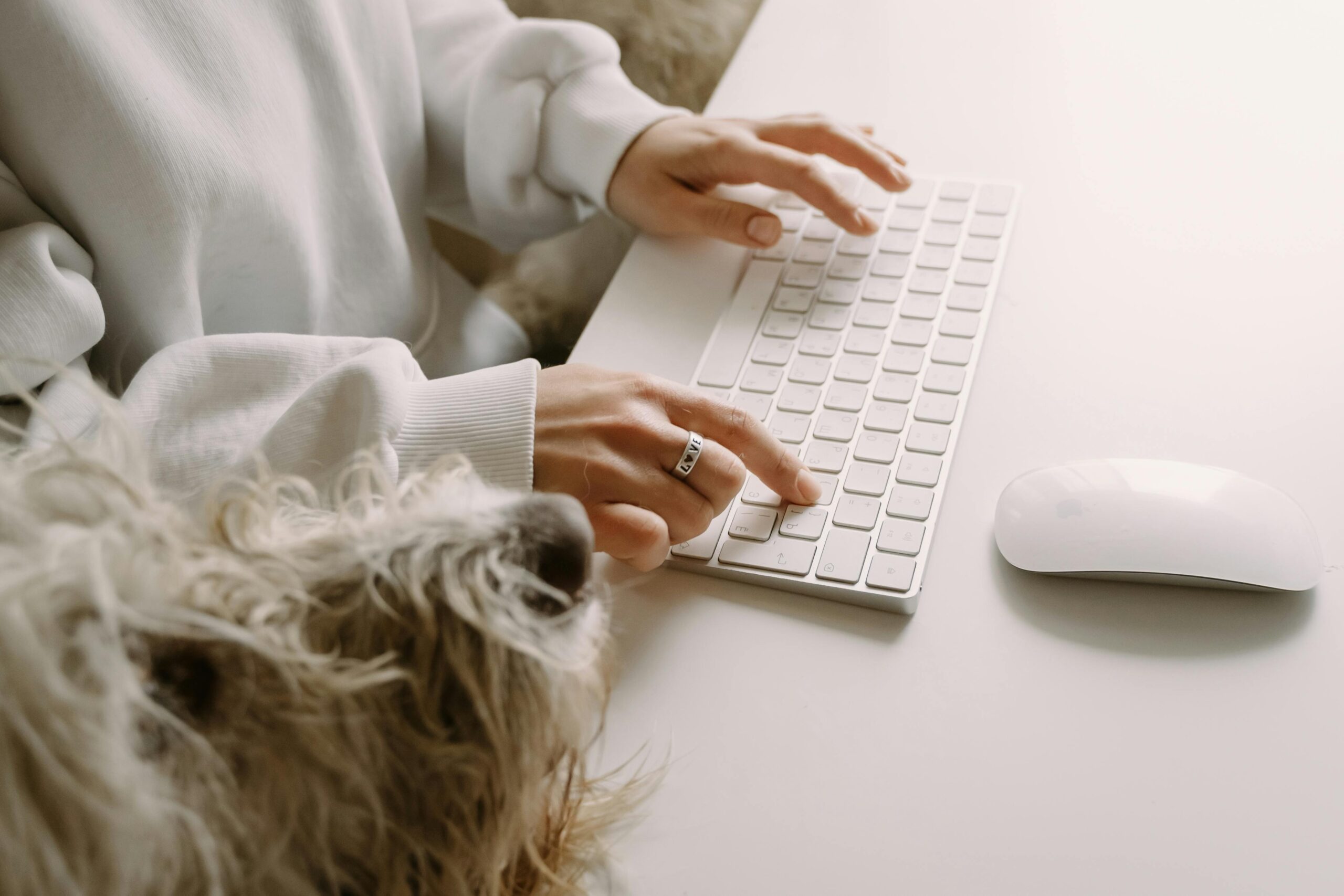 A person typing on a wireless keyboard with a fluffy dog nearby, showcasing companionship and modern technology.