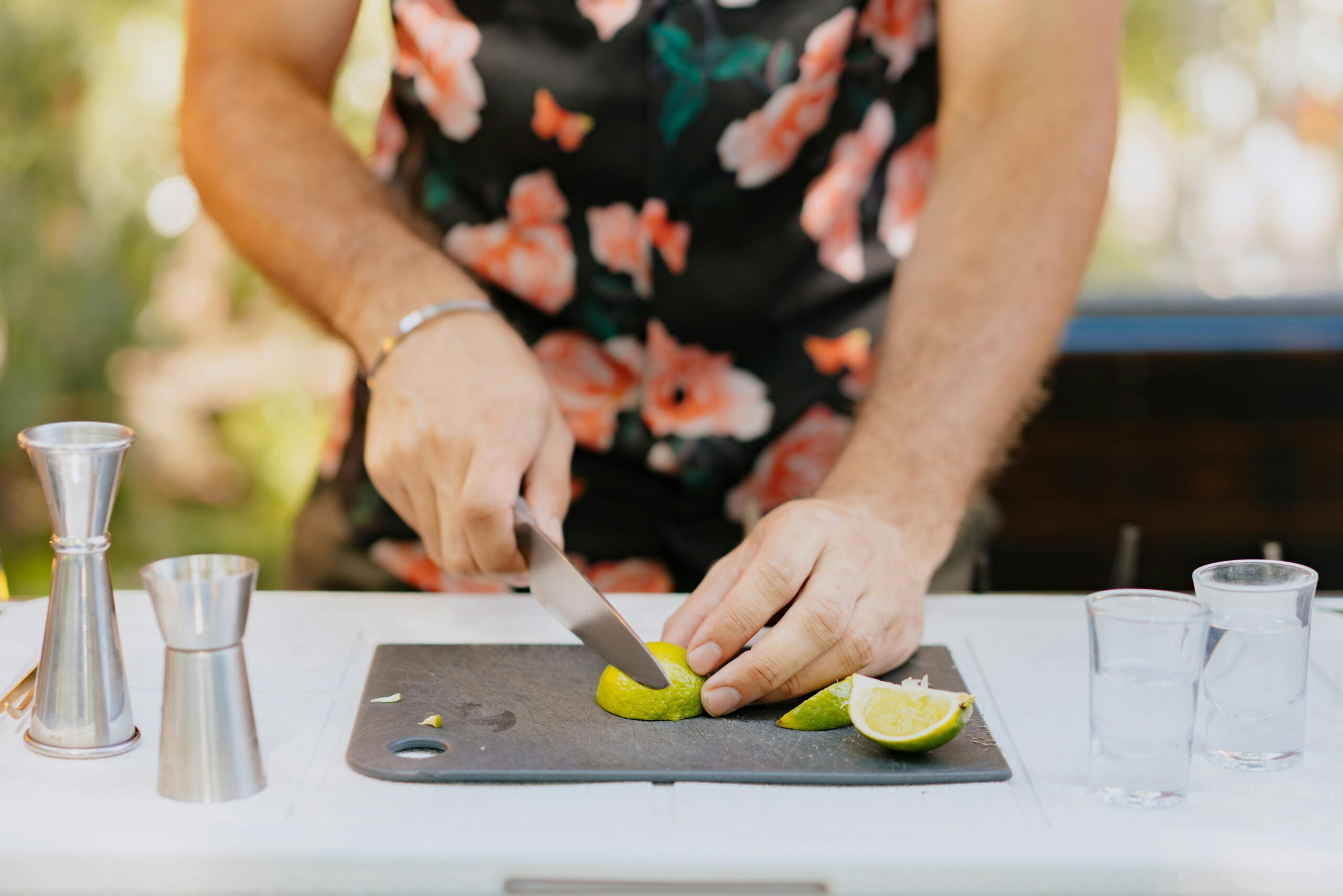 Photo of a man chopping lime for cocktails on an outdoor bar setup, with shot glasses nearby.