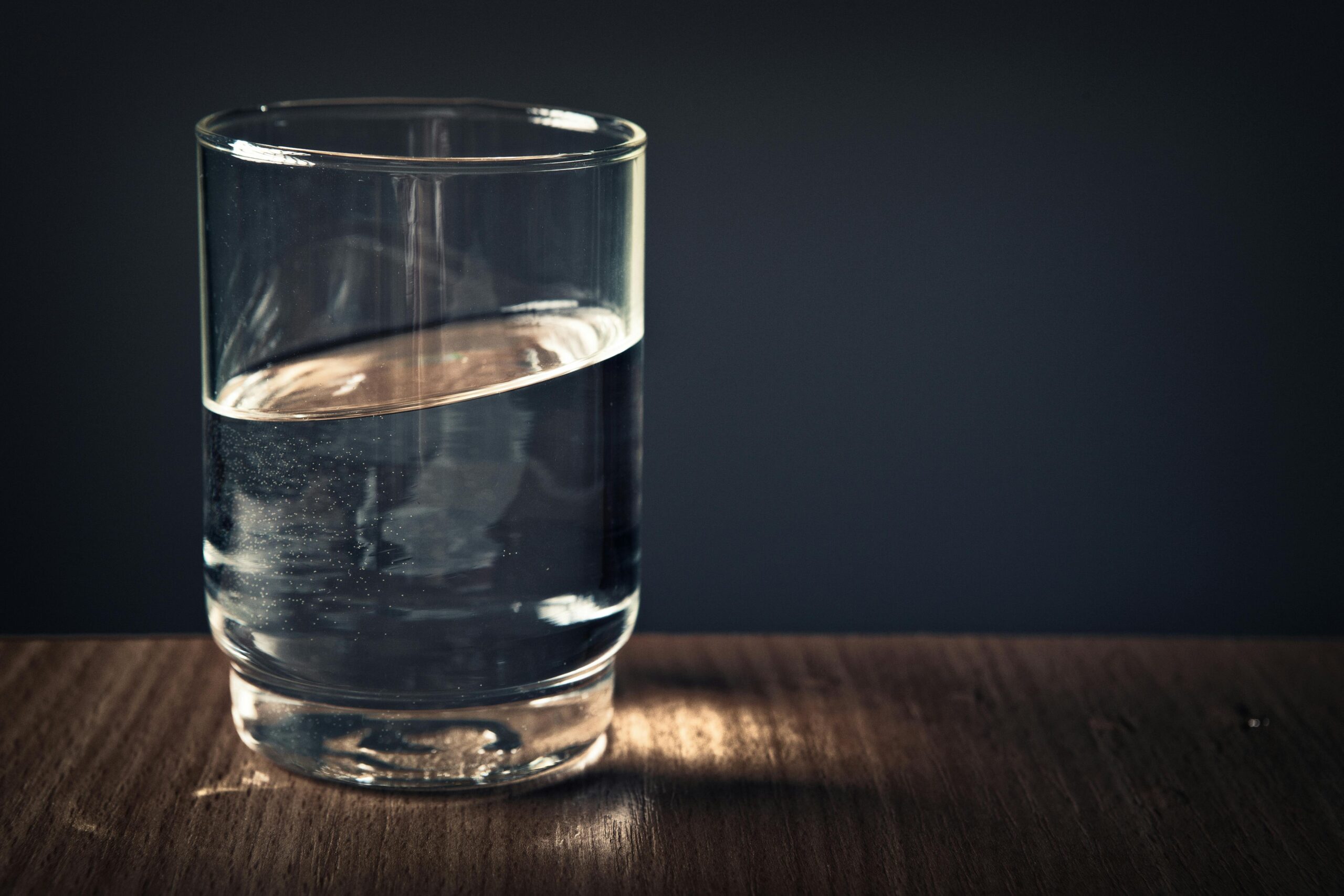 A clear glass of water sitting on a wooden table against a dark background.